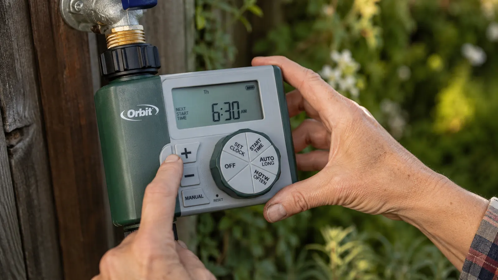 Hand pressing the buttons on the Orbit timer's LCD screen to set a morning watering schedule