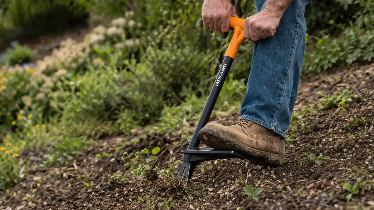Close-up of a boot pressed at an angle on the foot platform of the stand-up weed puller while working on a slightly sloped garden bed
