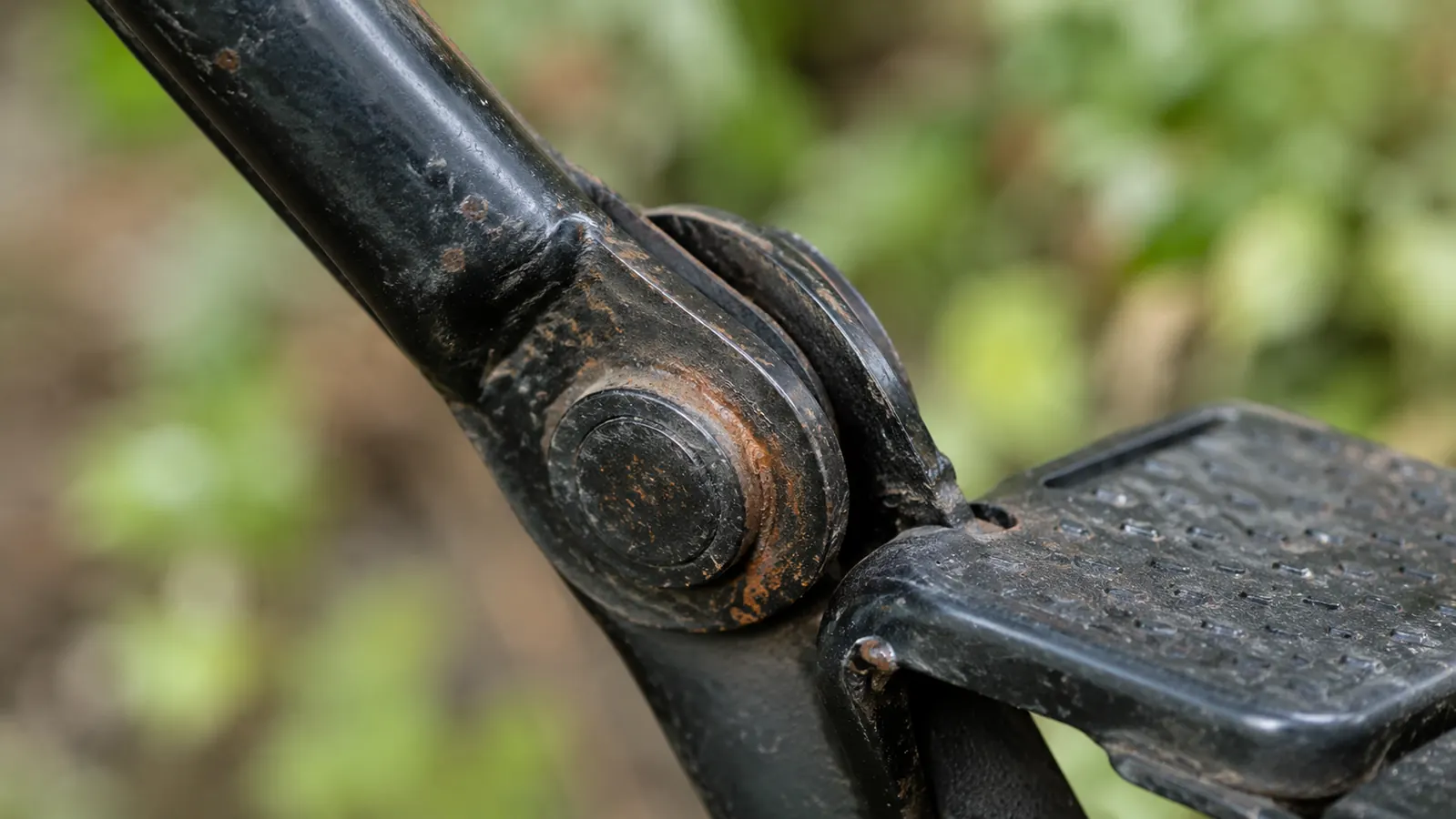 Close-up detail shot of a small rust spot forming on the metal pivot joint of the stand-up weed puller near the foot platform